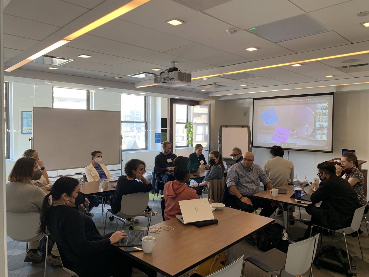 A group of hack the hackathon participants sitting around tables in a meeting room.