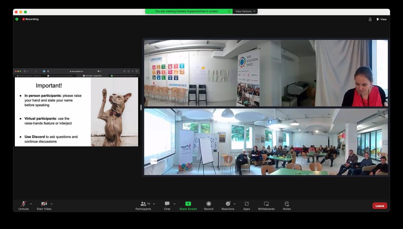 A screenshot of a screen showing a slide with important conference information, as well as a video of the speaker and a video of the room with in-person participants